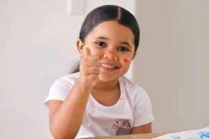 Smiling young girl with thumbs up fingerpainting